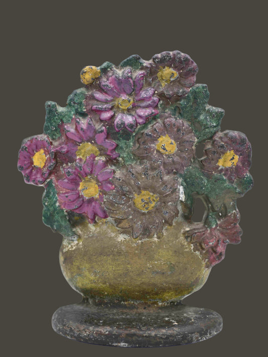 A vintage floral doorstop featuring pink and brown daisies in a gold vase with a white area in the center of the largest brown flower. The base is brown with light chipping, and the back is gold.