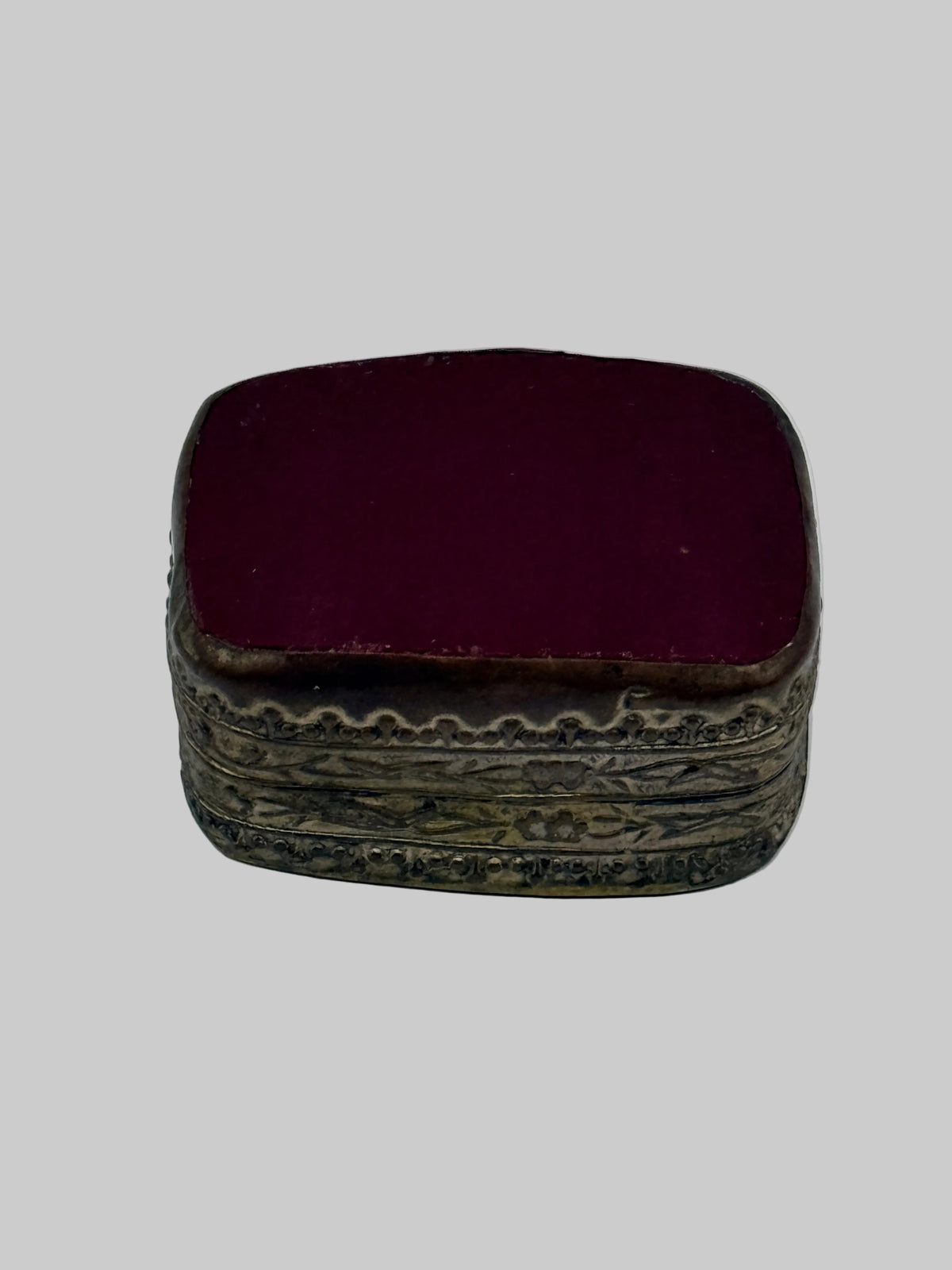 A small vintage jewelry box with a deep burgundy velvet-covered lid and an ornate, carved antique silver-tone metal base, shown on a plain light gray background.