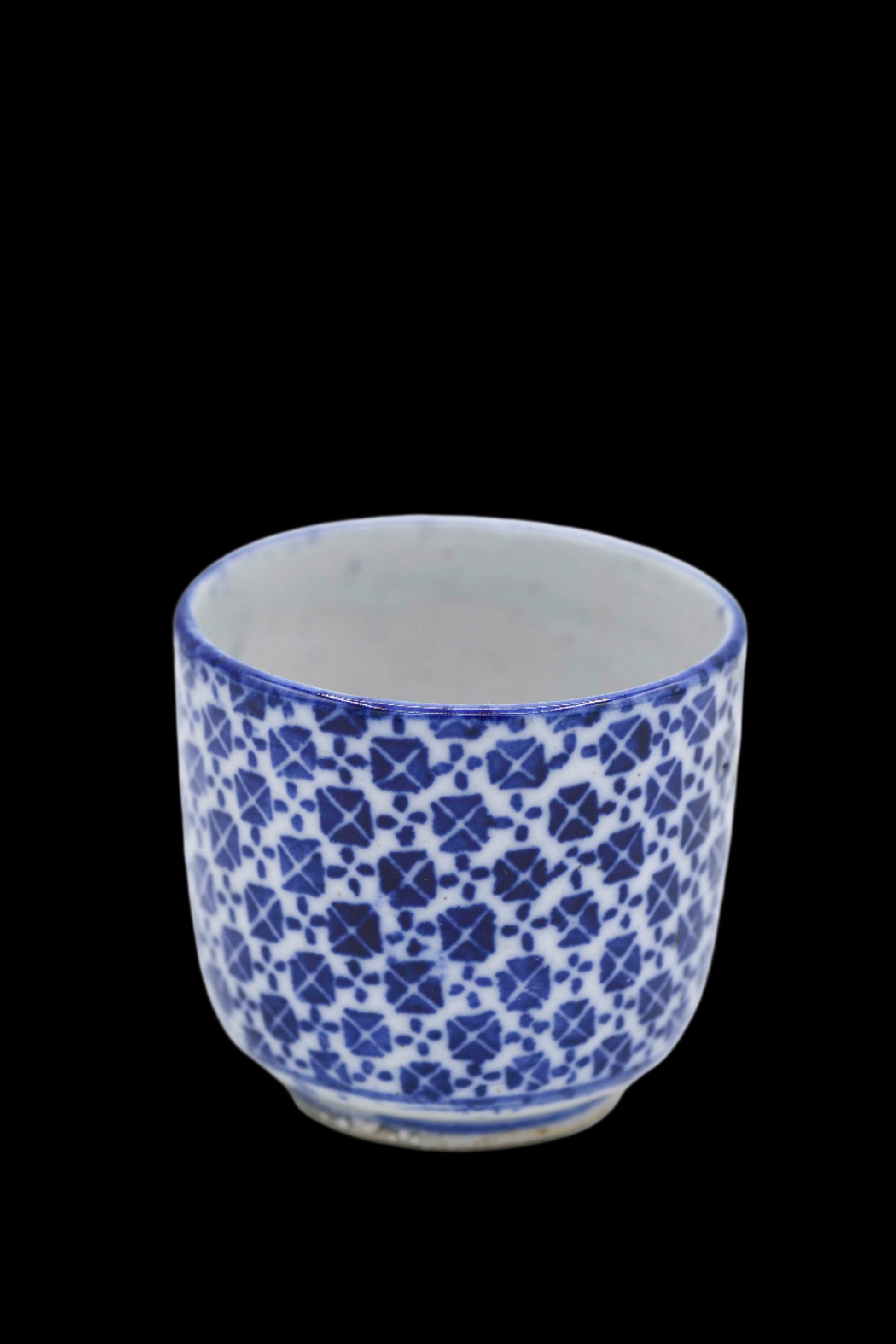 A small vintage blue and white geometric transferware teacup with a floral pattern, a creamy smooth interior, and a blue rim.