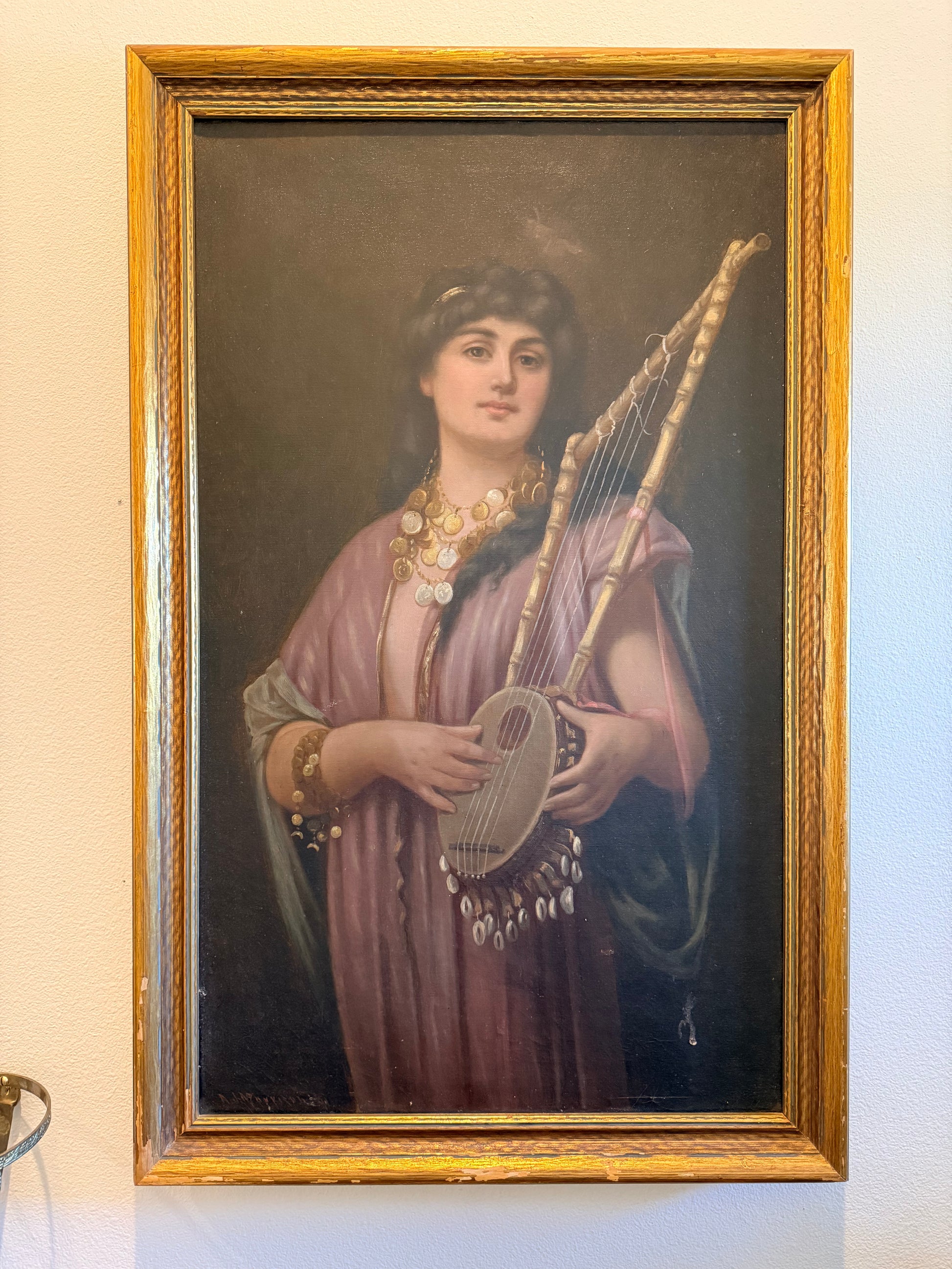 Portrait of a woman holding a harp in a gold frame on a beige wall.