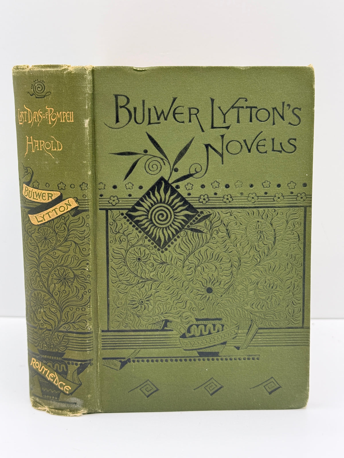 An antique hardcover book titled 'Bulwer Lyton's Novels' by Harold Bulwer, published by Routledge. The book features an olive green cloth binding with black embossed floral patterns and gold lettering on the spine.