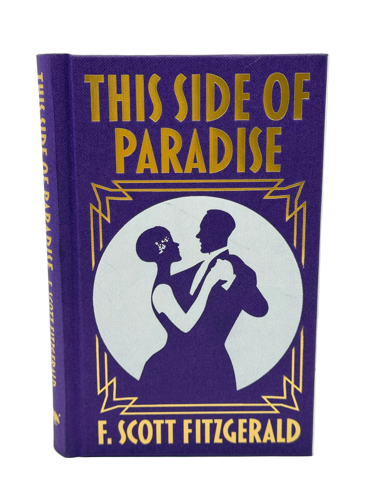 A hardcover book of F. Scott Fitzgerald's 'This Side of Paradise' with a purple cloth binding and gold lettering, featuring a white circular illustration of a dancing couple on the front cover.