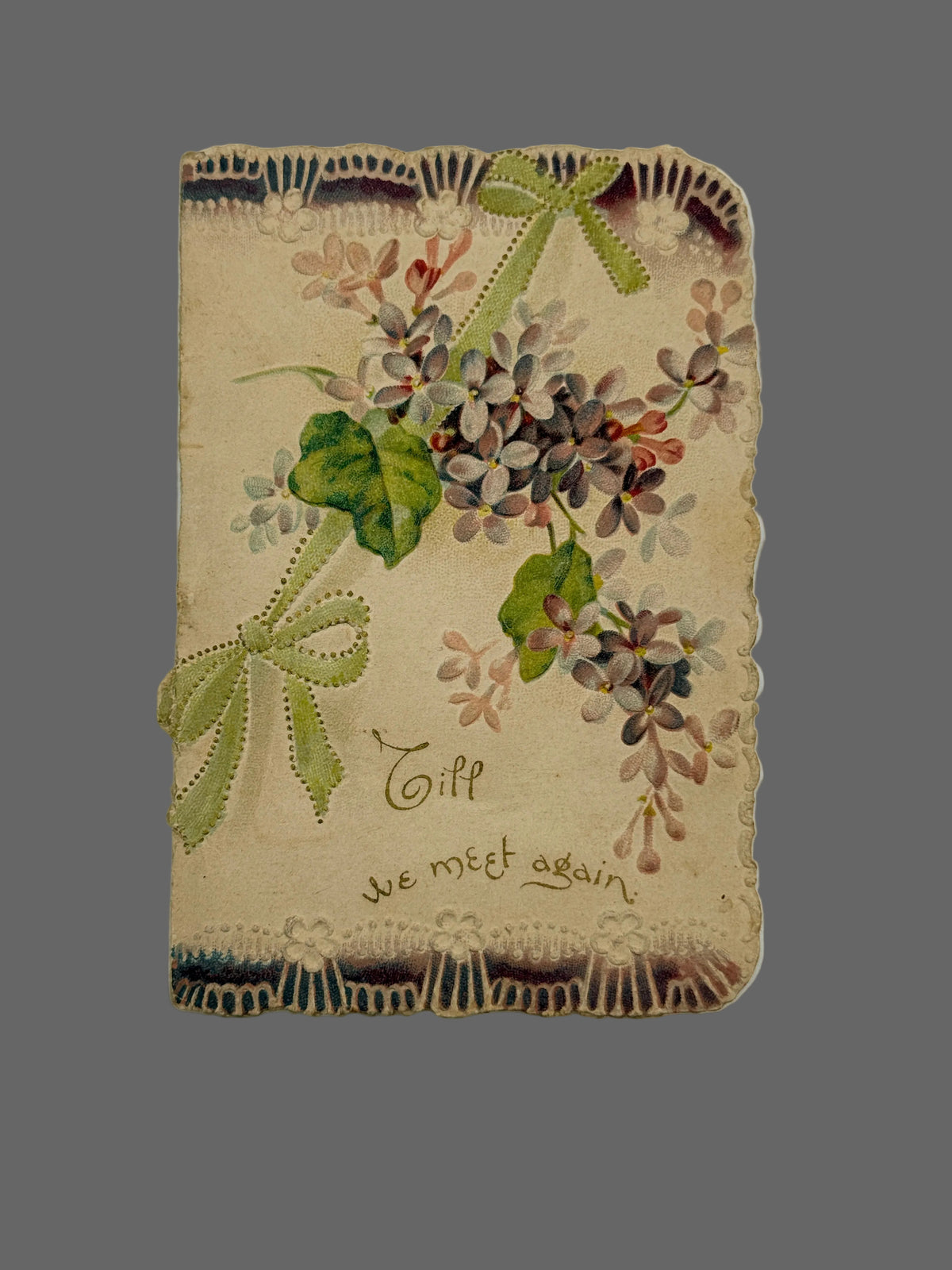 An antique-style decorative card or notebook cover with a vintage floral design, lace trim, green ribbon bows, and the handwritten text 'Till we meet again' on a light neutral background.