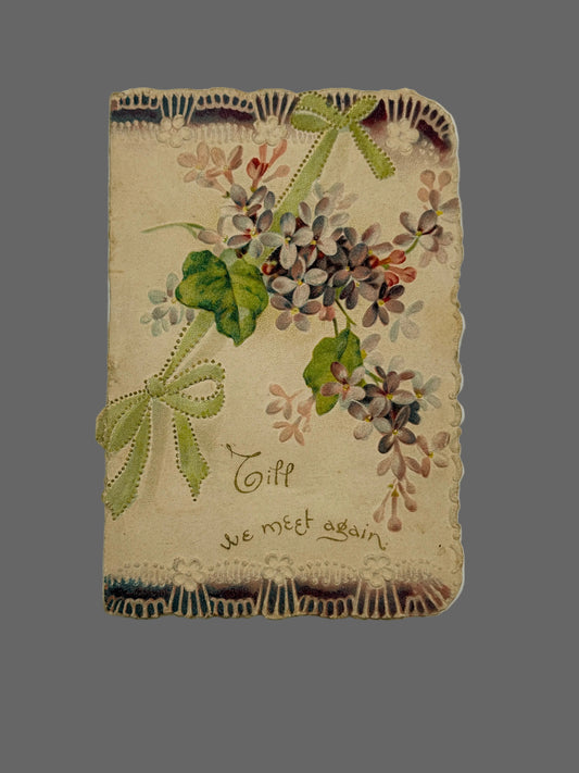 An antique-style decorative card or notebook cover with a vintage floral design, lace trim, green ribbon bows, and the handwritten text 'Till we meet again' on a light neutral background.