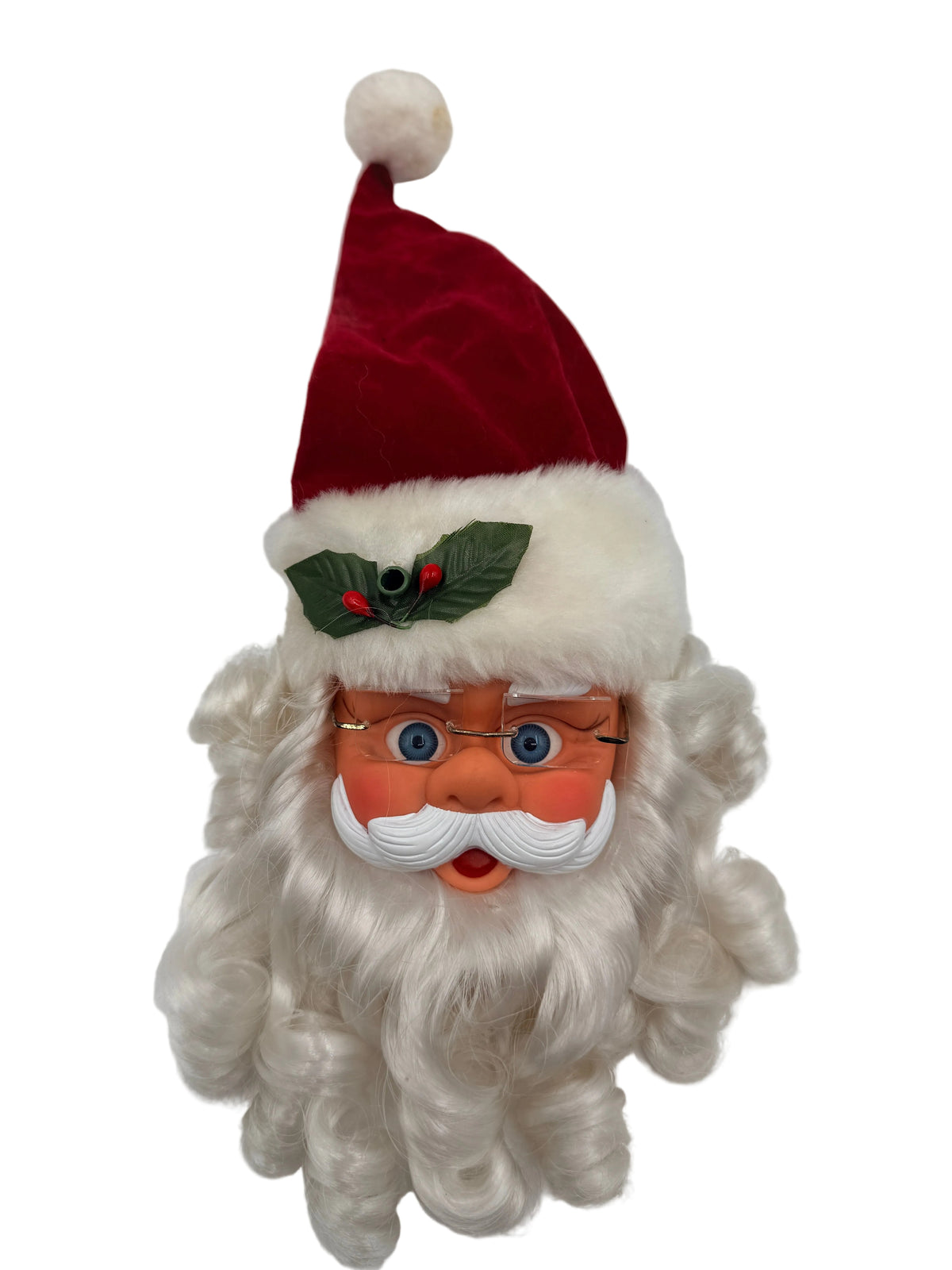 A vintage-style Santa Claus head decoration with a red velvet hat, white faux fur trim, a green holly accent, and a long curly white beard. The face has orange skin, blue eyes, and glasses.