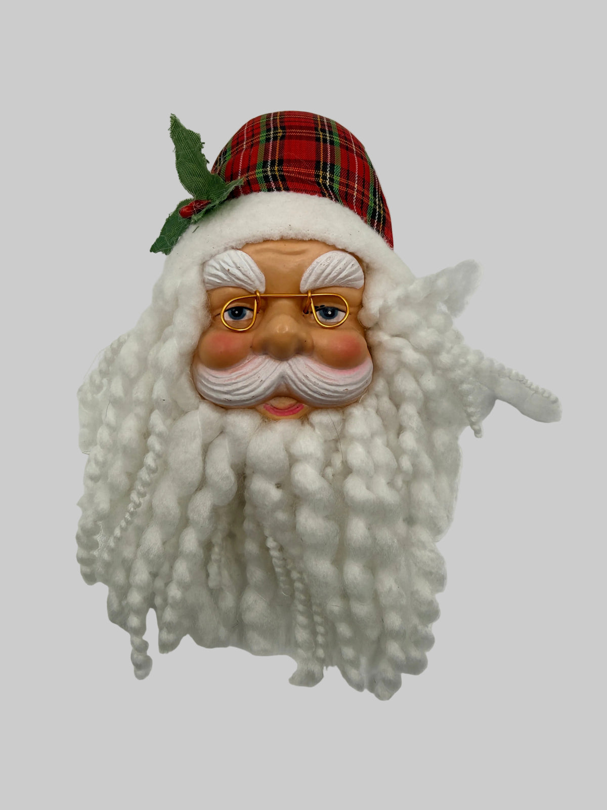 A vintage-style Santa Claus face mask or decorative headpiece with a long white curly beard, painted face, red plaid hat, and green holly accent, shown against a plain white background.