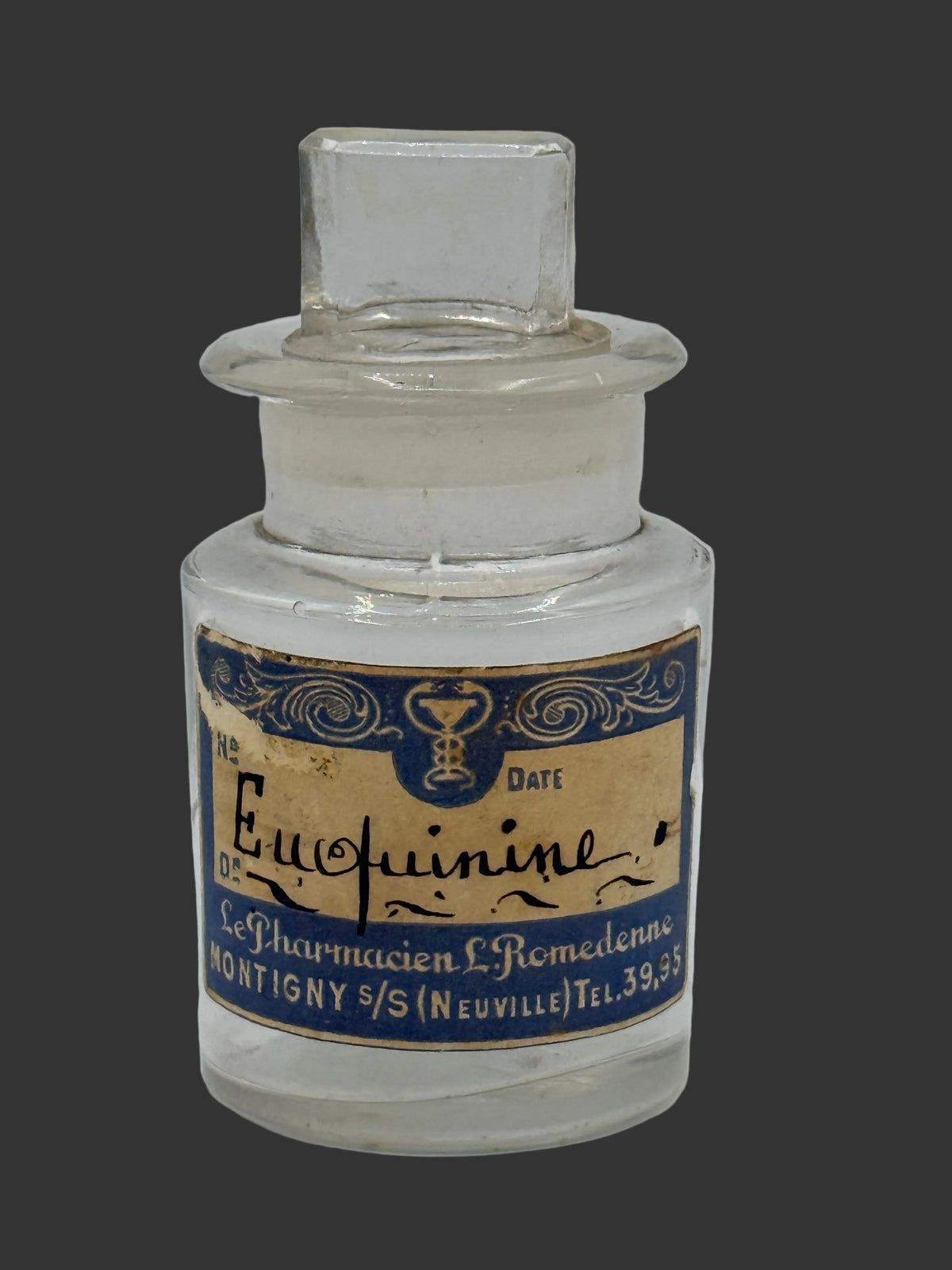 A vintage clear glass apothecary bottle with a stopper and a blue-and-gold label reading 'Euphorine' and 'Le Pharmacien R. Romedenne', photographed against a plain light gray background.