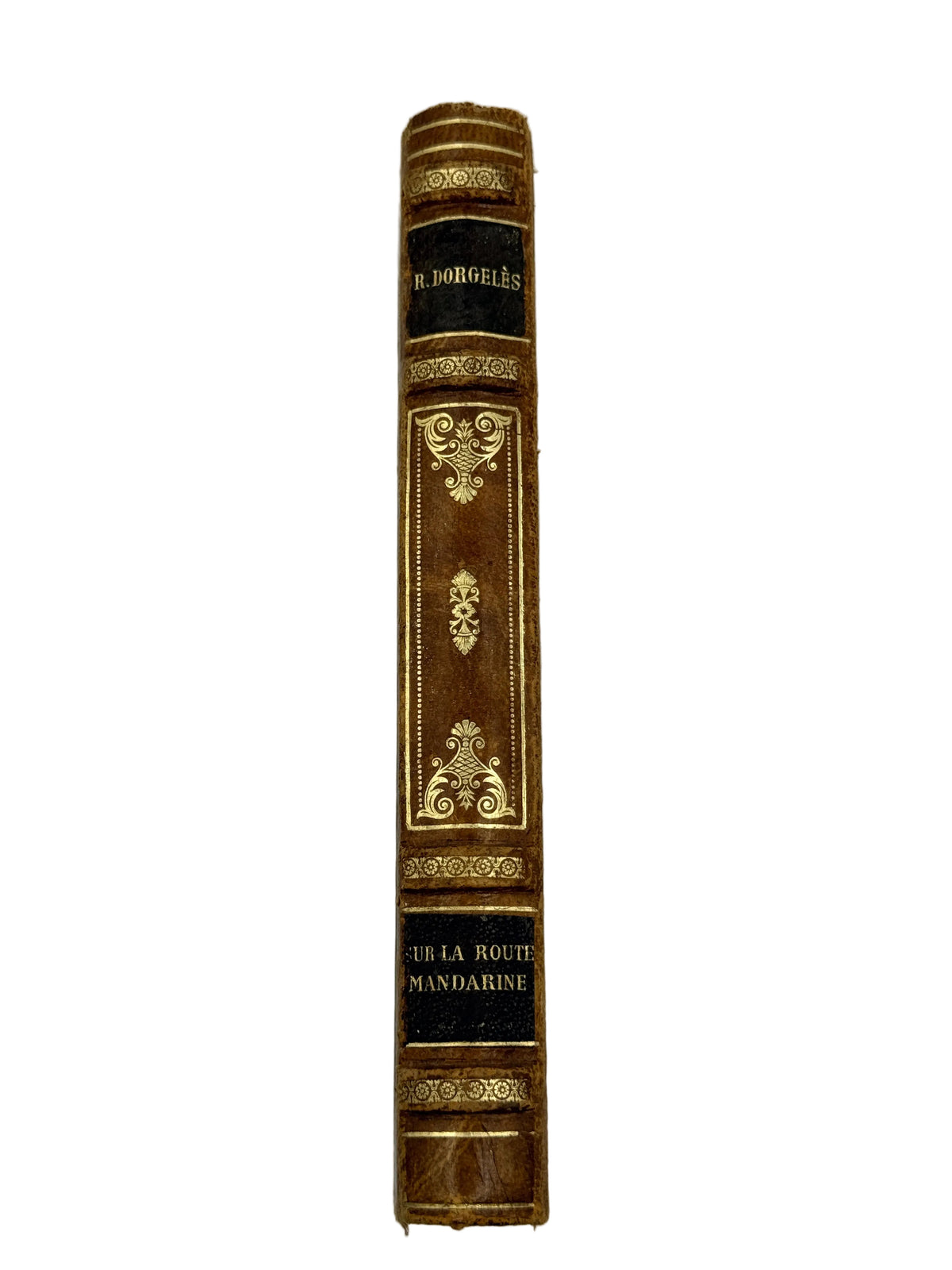 A single antique book spine standing upright against a plain light gray background. The spine is brown with ornate gold embossed decoration and black bands containing gold text, including the visible title 'Sur la Route Mandarine' and author name 'R.
