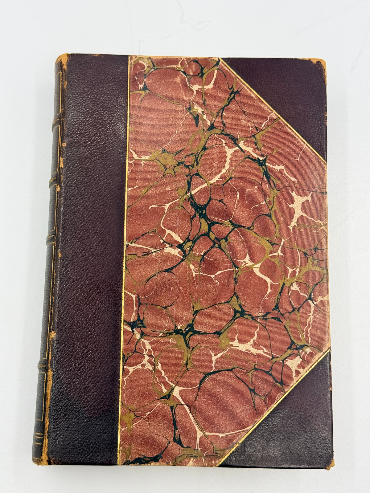 An antique hardcover book with a dark brown leather spine and a marbled paper cover in reddish-brown, beige, and black with gold veining.
