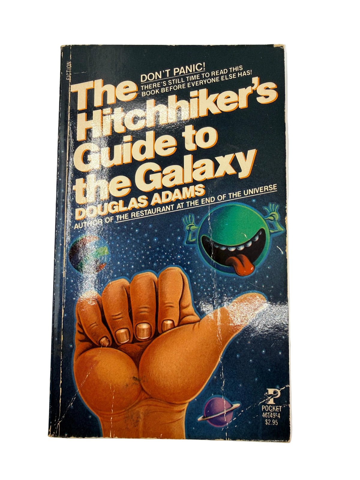 Vintage paperback book of The Hitchhiker's Guide to the Galaxy by Douglas Adams, featuring a dark blue space cover with a large orange hand and a green mouth graphic.
