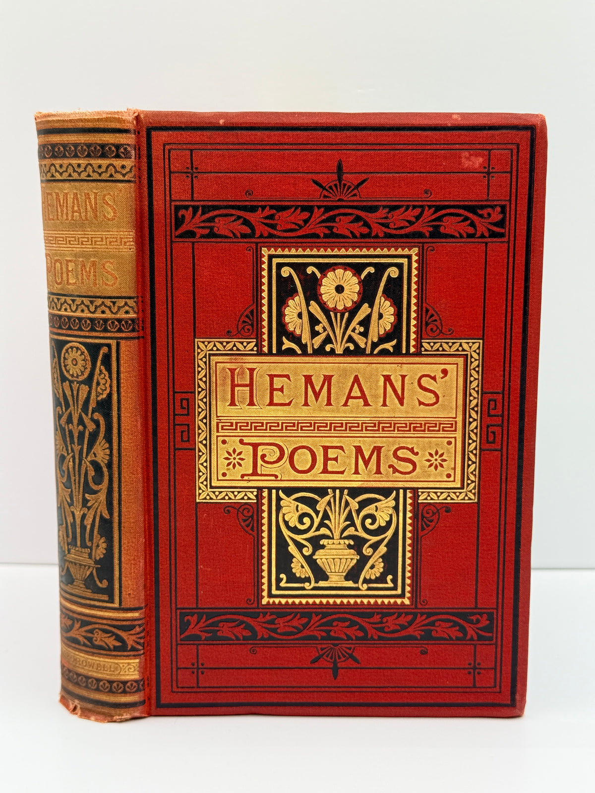 A vintage hardcover book titled 'Hemans' Poems' with a red cloth cover and gold embossed floral and decorative border details, shown standing upright with the spine visible against a plain light background.