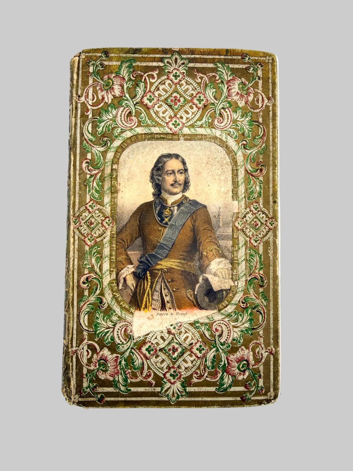 An antique decorative portrait card or print featuring a man in historical dress, surrounded by ornate floral and scrollwork borders in muted green, gold, and pink tones, shown against a plain white background.