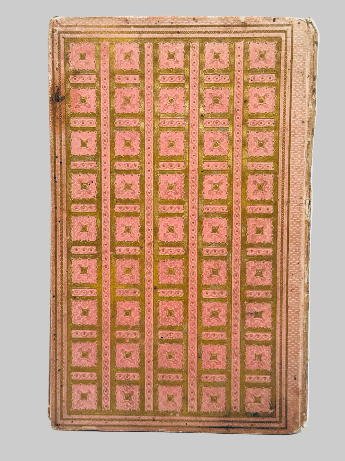 An antique book or notebook showing the back cover, decorated with a repeating pattern of pink and gold geometric squares and bordered by a matching pink and gold frame.