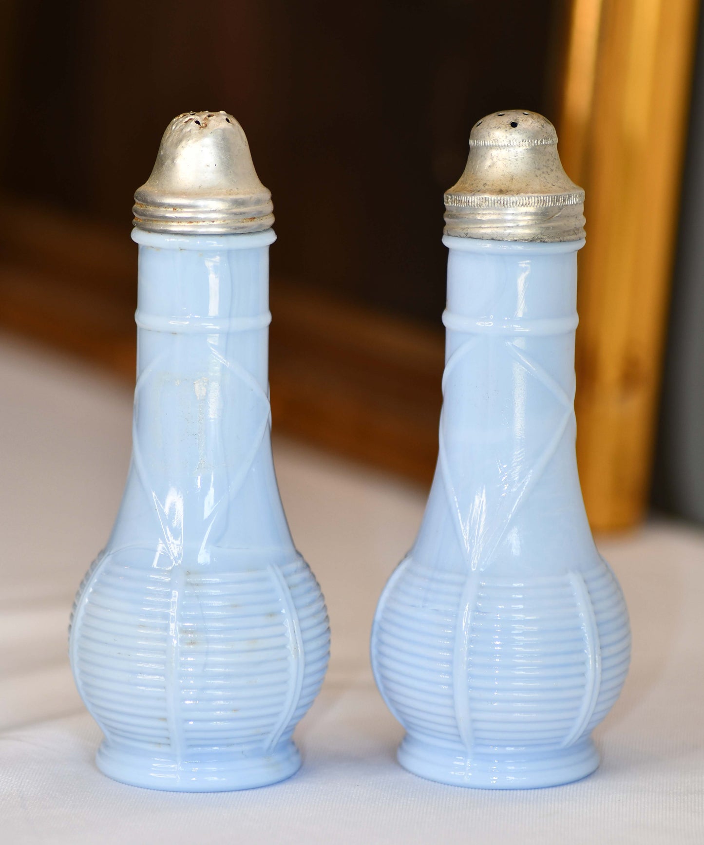 Two blue glass salt and pepper shakers with gold lids on a neutral background.