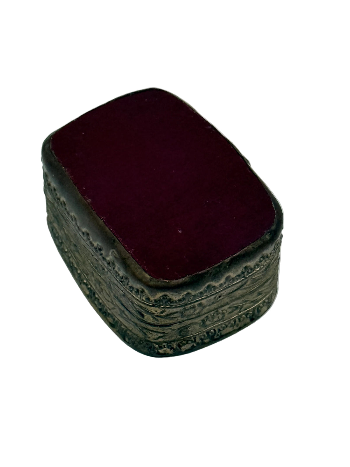 A small rectangular vintage box with a dark burgundy velvet-covered lid and an ornate silver-toned metal base decorated with embossed floral patterns, set against a plain light gray background.