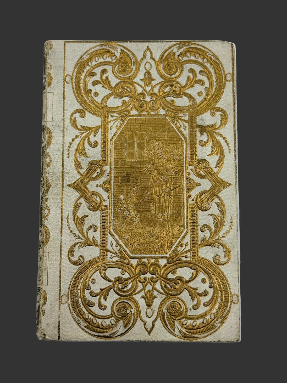 An antique book or journal with an ornate gold foil design on a cream-colored cover, photographed flat against a light background.